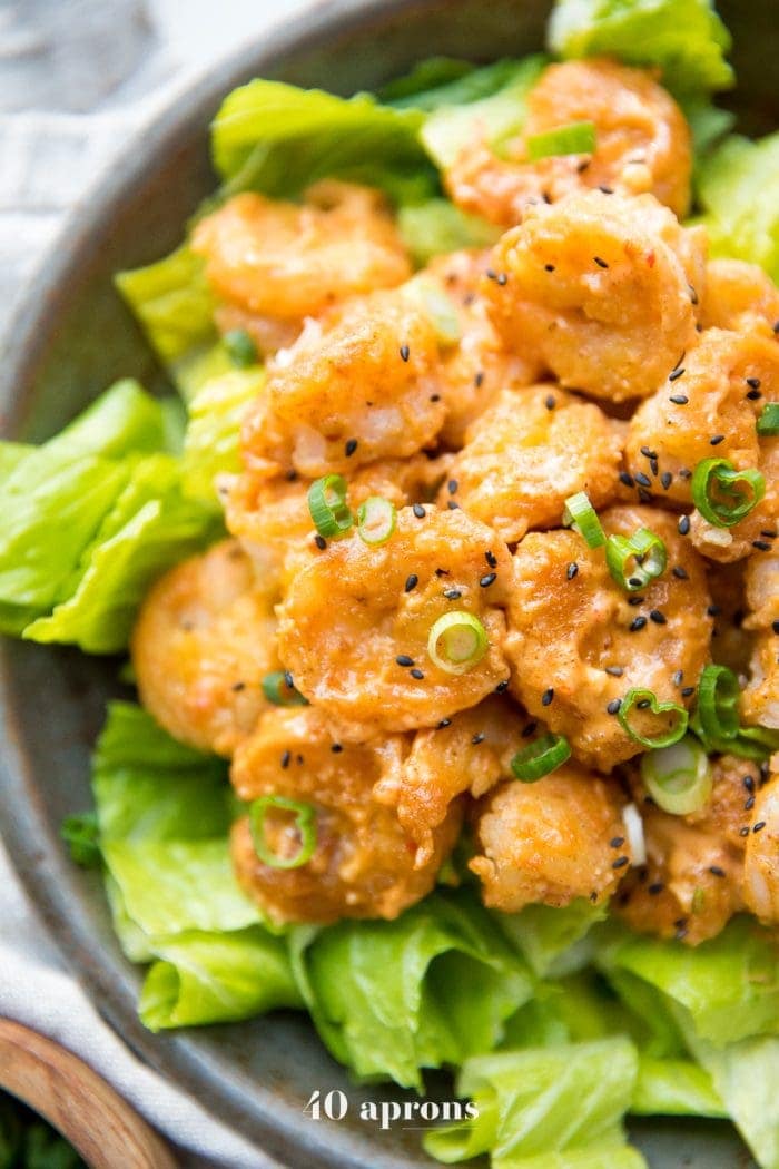 Whole30 bang bang shrimp topped with green onions and sesame seeds on a bed of romaine lettuce