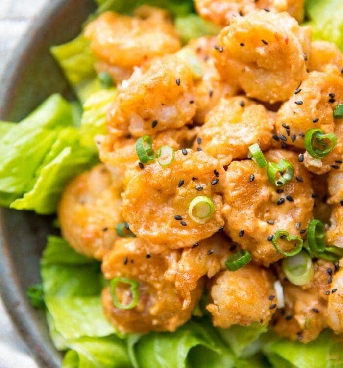 Whole30 bang bang shrimp topped with green onions and sesame seeds on a bed of romaine lettuce