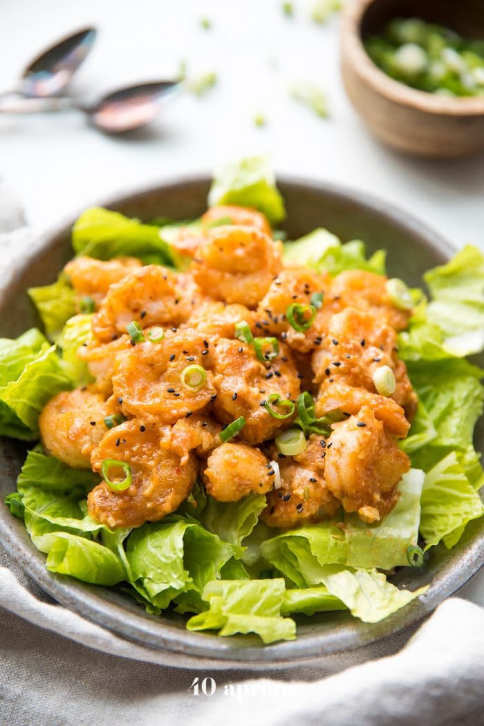 Whole30 bang bang shrimp topped with green onions and sesame seeds on a bed of romaine lettuce