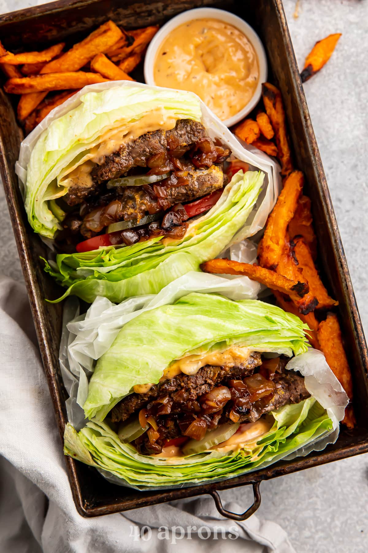 Overhead view of two Whole30 In-n-out burgers in a serving tray with sweet potato fries and animal sauce