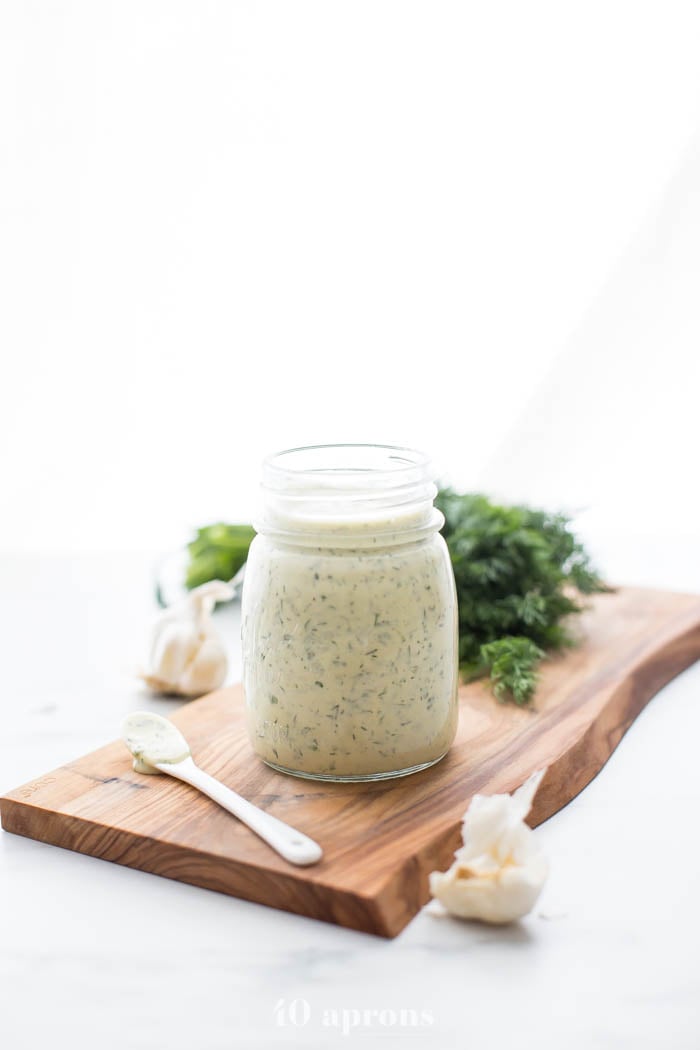 Whole30 ranch dressing in a jar on a board with fresh herbs in background