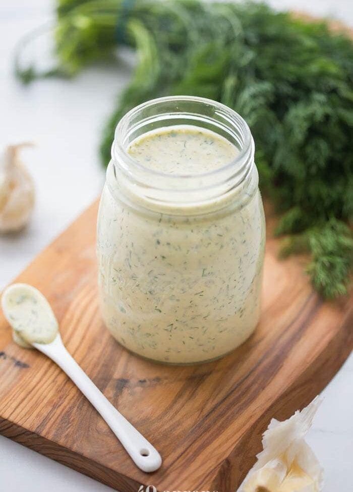Whole30 ranch dressing in a jar on a board with fresh herbs in background