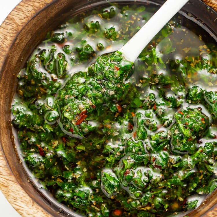 Overhead view of Texas de Brazil chimichurri sauce in a small wooden bowl with a spoon.