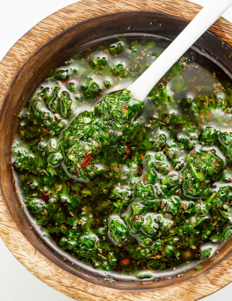 Overhead view of Texas de Brazil chimichurri sauce in a small wooden bowl with a spoon.
