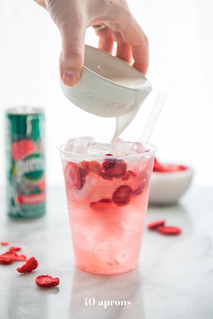 coconut milk in a white bowl is poured into strawberry refresher drink