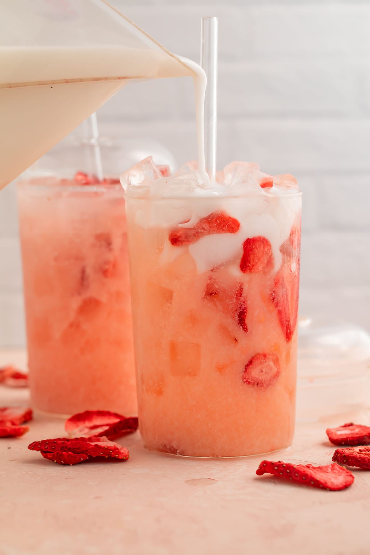 Milk being poured into a glass holding a pink drink copycat with freeze-dried strawberries.