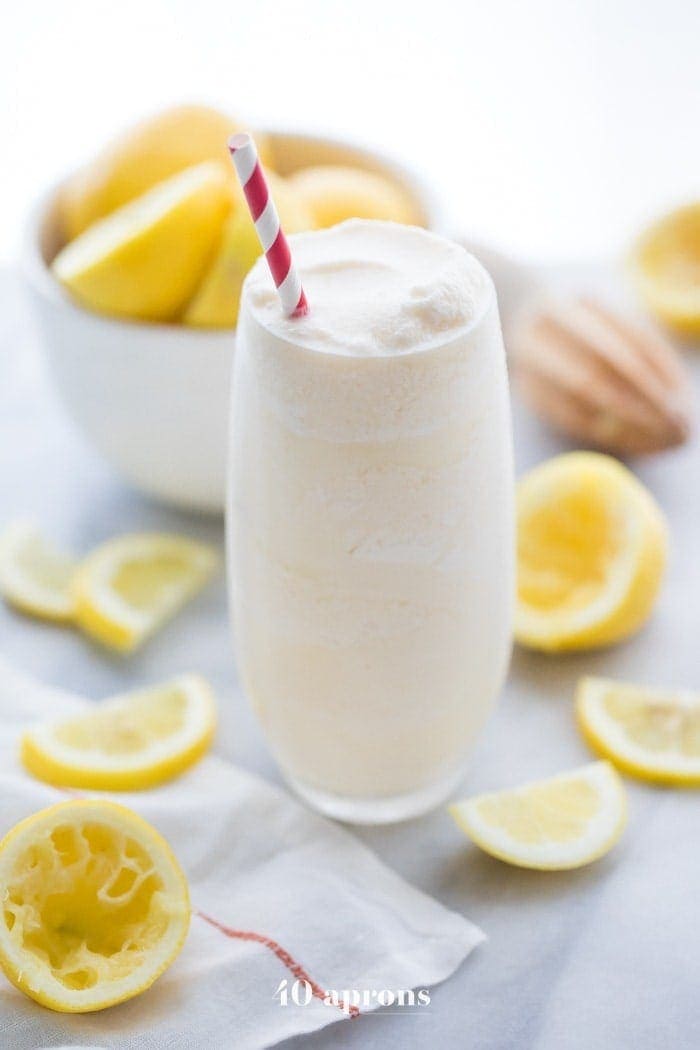 Healthy frosted lemonade in a glass with a straw and lemons in the background