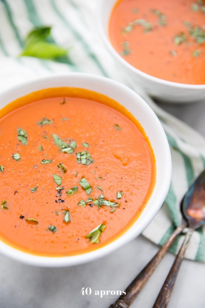 Perfect Whole30 Instant Pot tomato soup (vegan) served in two white bowls placed on a white and green striped tablecloth - overhead shot