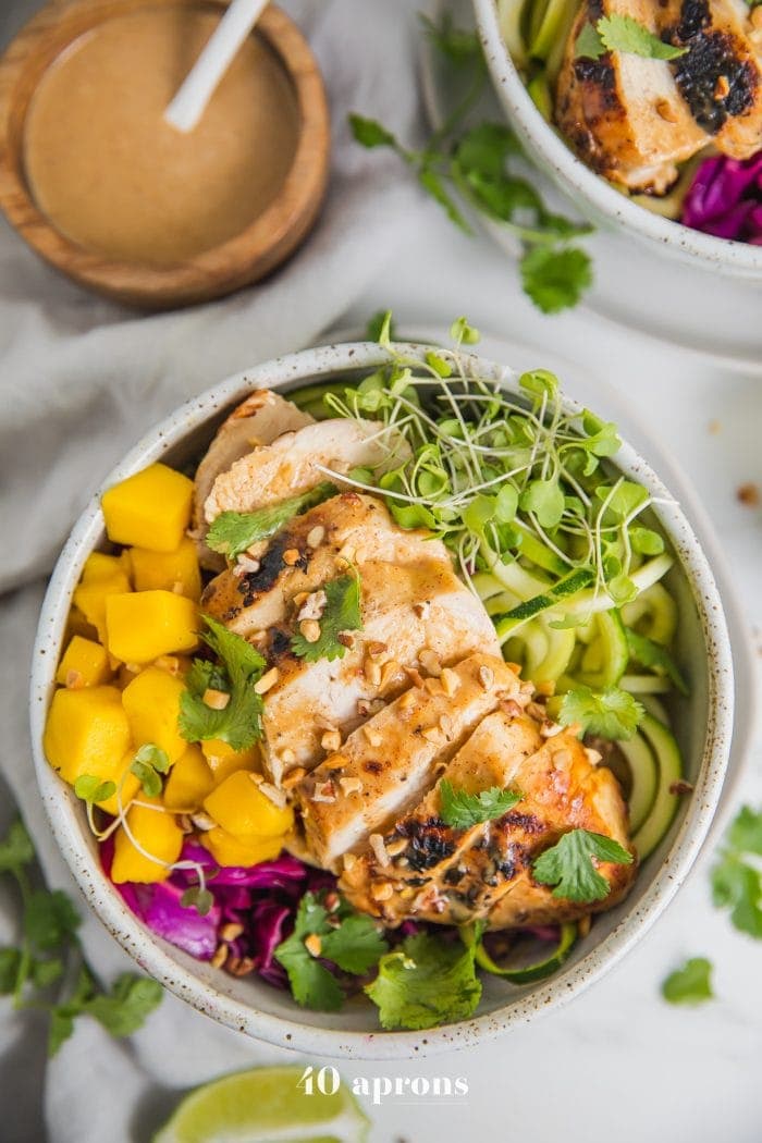 Whole30 Thai chicken zoodle bowls with "peanut sauce" in a bowl with garnishes
