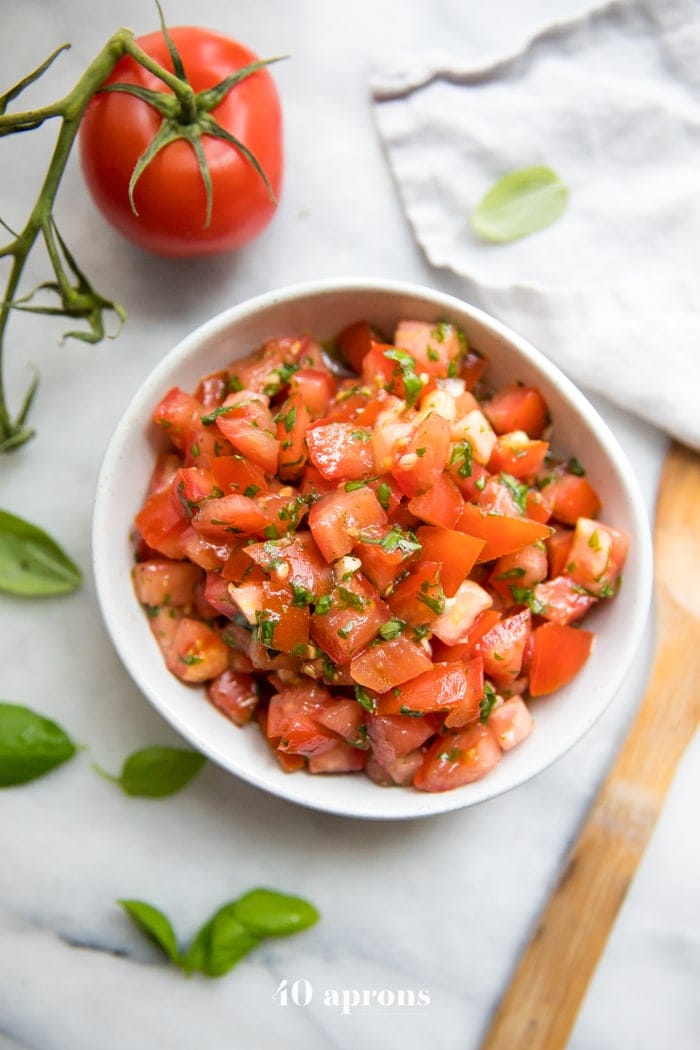 Bowl de bruschetta fresca com tomate, manjericão e alho, tomate e manjericão fresco ao lado