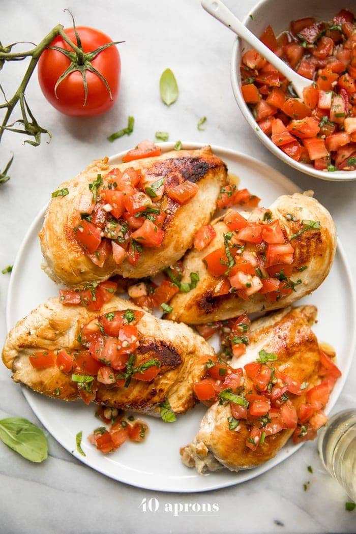 Pollo alla bruschetta su un piatto con basilico fresco, bruschetta e altro pollo alla bruschetta sullo sfondo