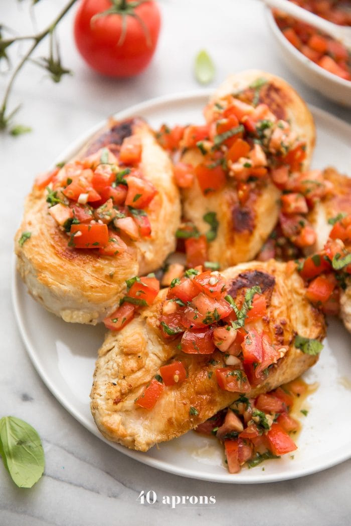 Pollo a la bruschetta en un plato con albahaca fresca, bruschetta, y más pollo a la bruschetta en el fondo