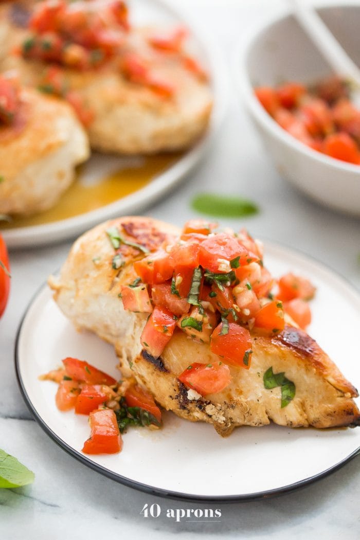 Pollo bruschetta en un plato con albahaca fresca, bruschetta, y más pollo bruschetta en el fondo