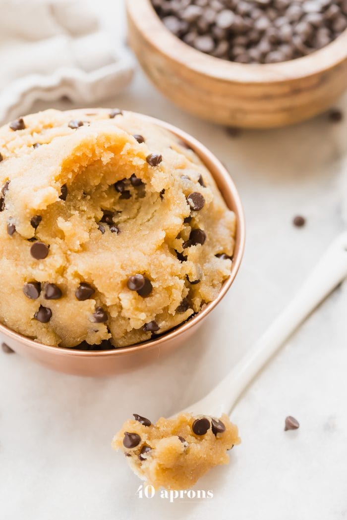 Vegan healthy cookie dough in a copper bowl with a bite taken out and a bowl of chocolate chips in the corner