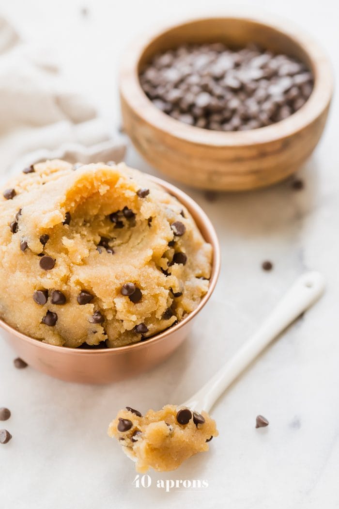 Vegan healthy cookie dough in a copper bowl with a bite taken out and a bowl of chocolate chips in the corner