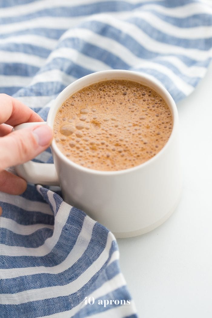 Hand holding a mug of miracle maca latte with a blue-striped towel