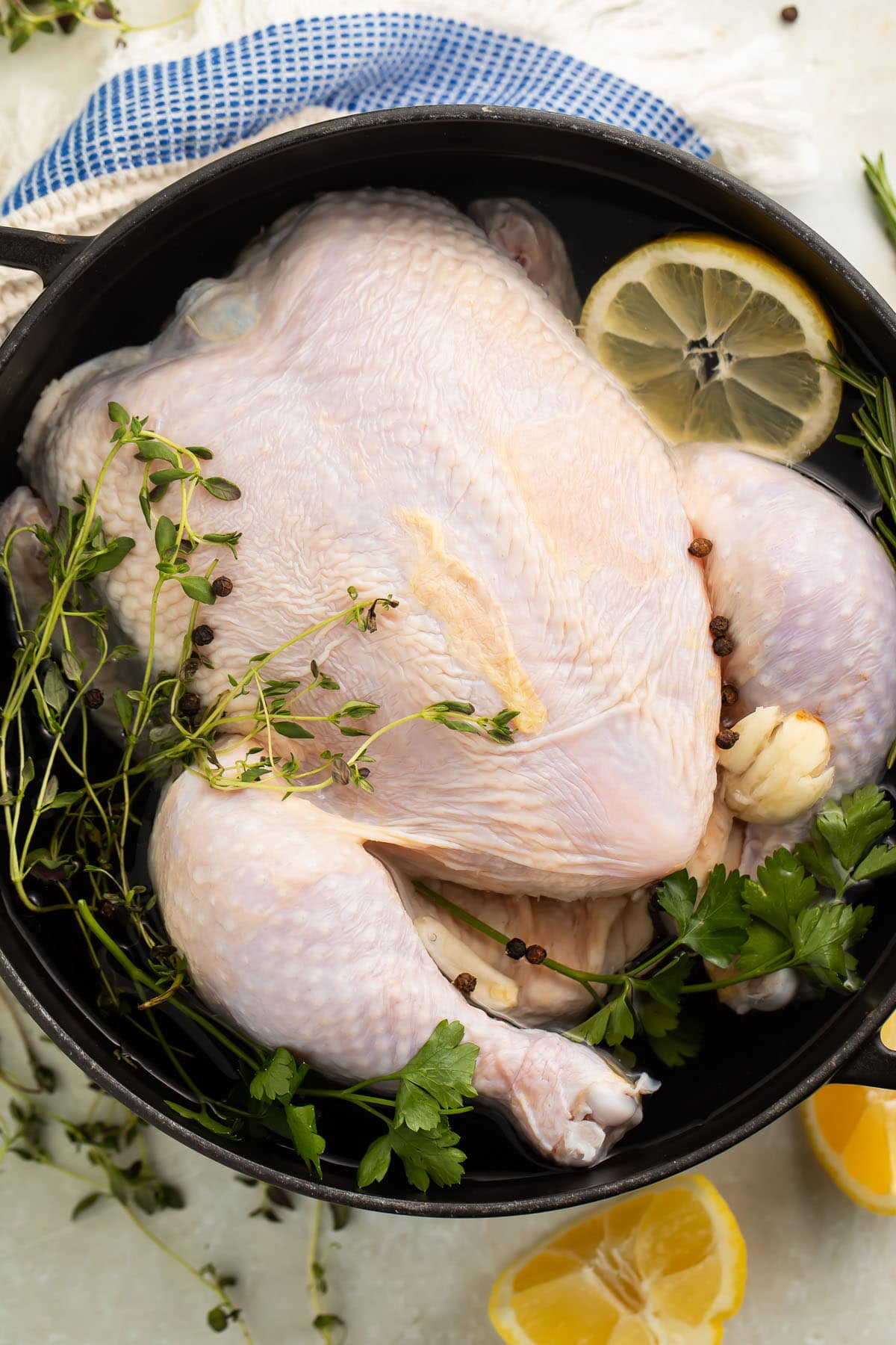 A whole, uncooked chicken in a large pot filled with a quick chicken brine of water, lemon, and herbs.