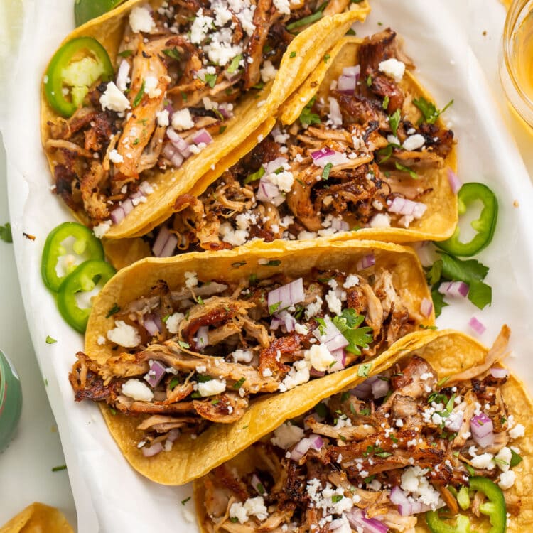 Four slow cooker carnitas tacos arranged on a large oval platter.