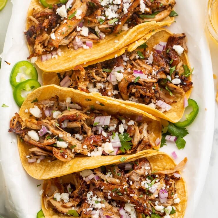 Four slow cooker carnitas tacos arranged on a large oval platter.