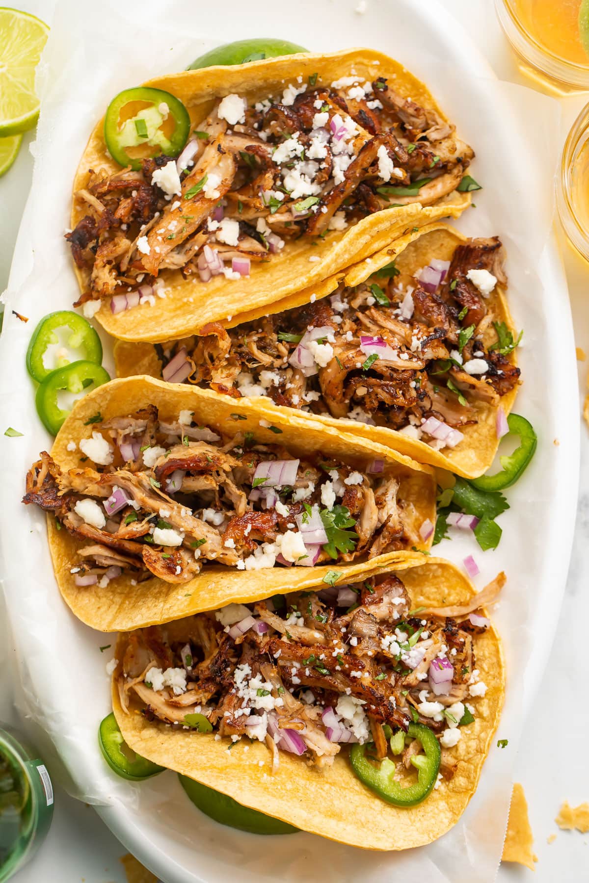 Four slow cooker carnitas tacos arranged on a large oval platter.