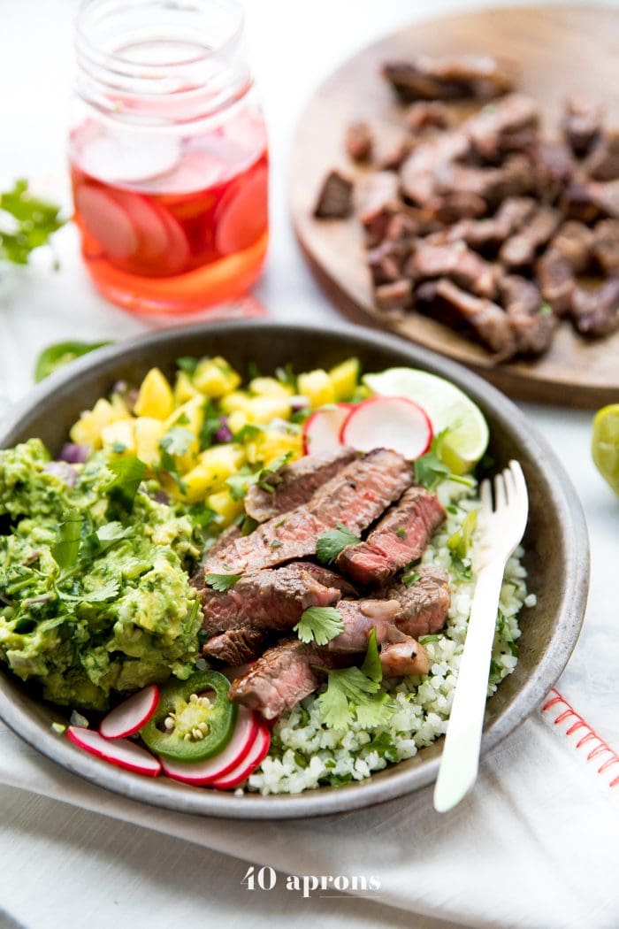 Whole30 steak taco bowls with steak, guacamole, pineapple salsa, pickled radish, and cauliflower rice