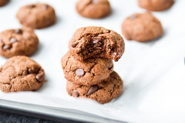 3 stacked Paleo Double Chocolate Fudge Cookies on a parchment paper-lined tray with more cookies in the background.