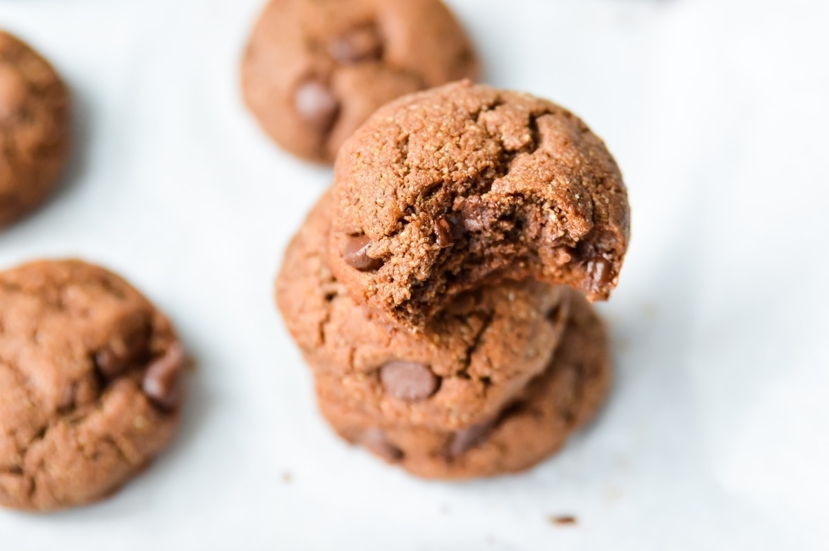 a stack of Paleo Double Chocolate Fudge Cookies on a lined baking tray with a bit taken from the top one.