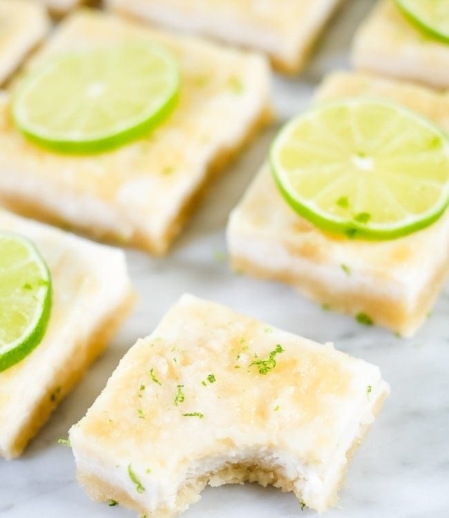Paleo Lime Bars on a white marble countertop with a bite taken out of the front.