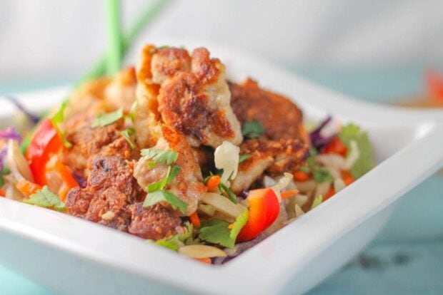 Paleo Sesame Chicken served on chopped Asian vegetables in a white bowl.