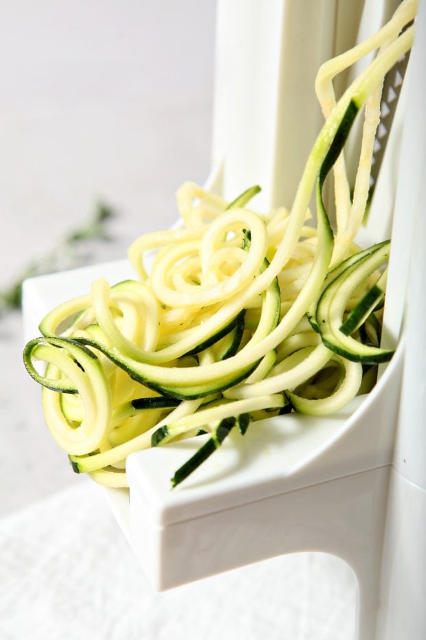 zucchini being cut into zucchini noodles with a spiralizer
