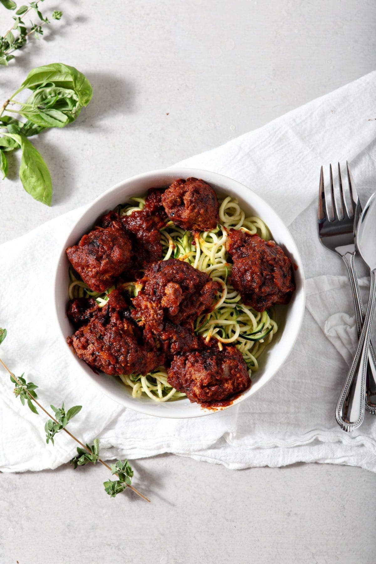 Whole30 Spaghetti and Meatballs served over zucchini noodles in a white bowl on a white tablecloth.