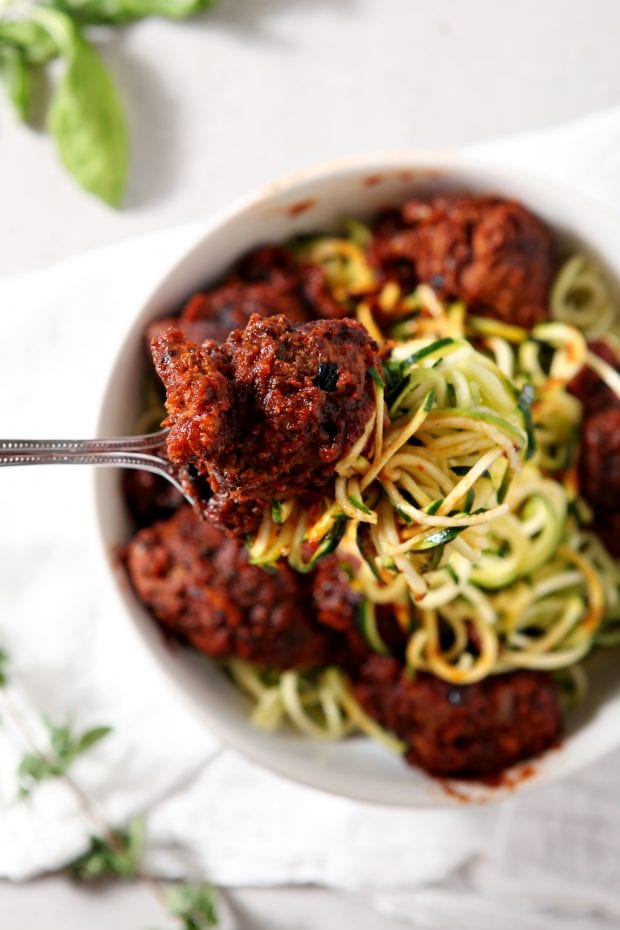 a fork full of Whole30 Spaghetti and Meatballs with balanced over a white bowl with more zucchini noodles and meatballs.