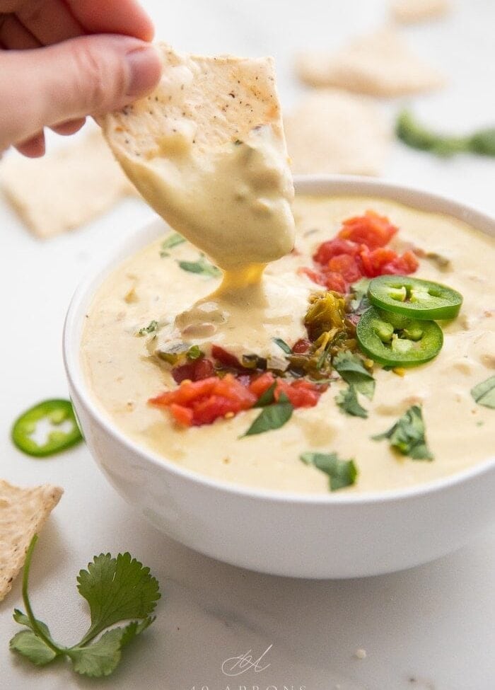 A chip dipping in a bowl of vegan queso
