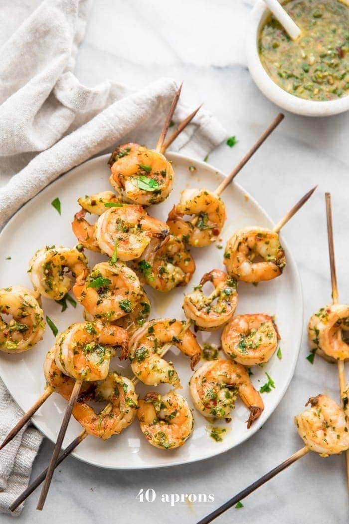 Quick Whole30 chimichurri shrimp skewers on a plate with a bowl of chimichurri