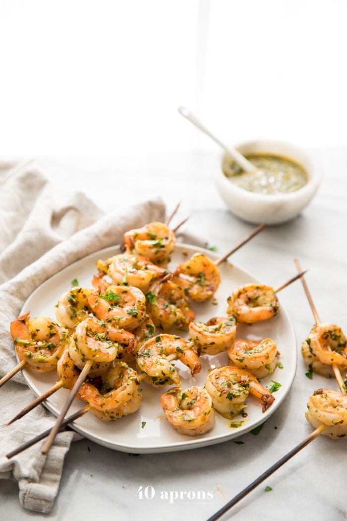 Quick Whole30 chimichurri shrimp skewers on a plate with a bowl of chimichurri