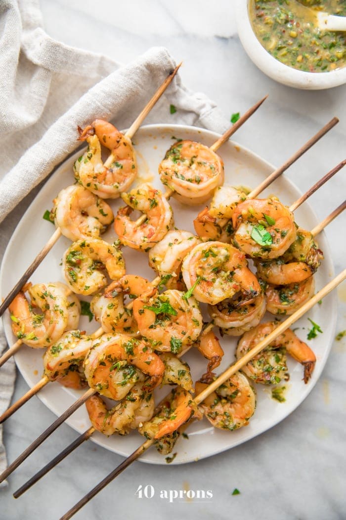 Quick Whole30 chimichurri shrimp skewers on a plate with a bowl of chimichurri