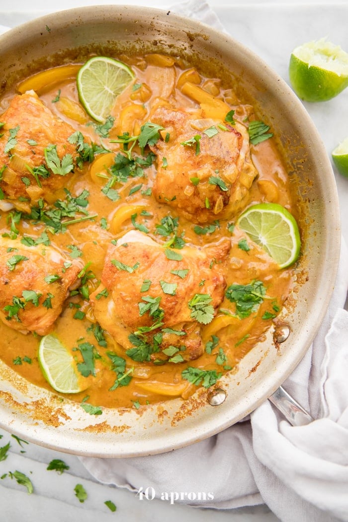 Coconut curry turmeric chicken in a pan with cilantro garnish and a lime to the side