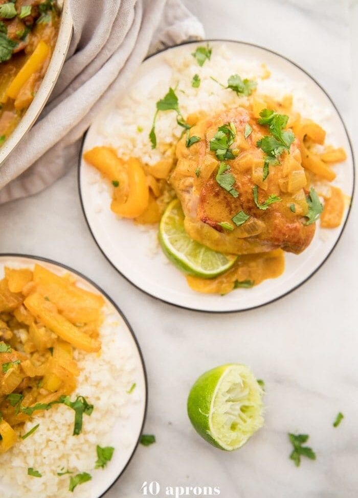 Coconut curry turmeric chicken on a plate with cilantro garnish and a lime to the side