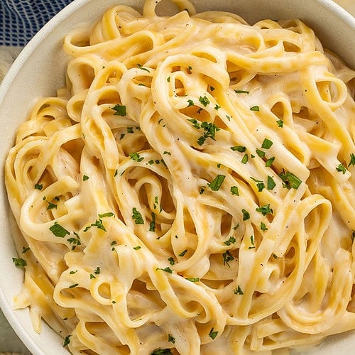 A bowl of creamy cottage cheese alfredo on fettuccine garnished with chopped parsley.