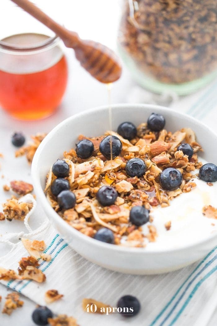 Bowl of the crunchy paleo granola recipe over yogurt, topped with blueberries and a drizzle of honey
