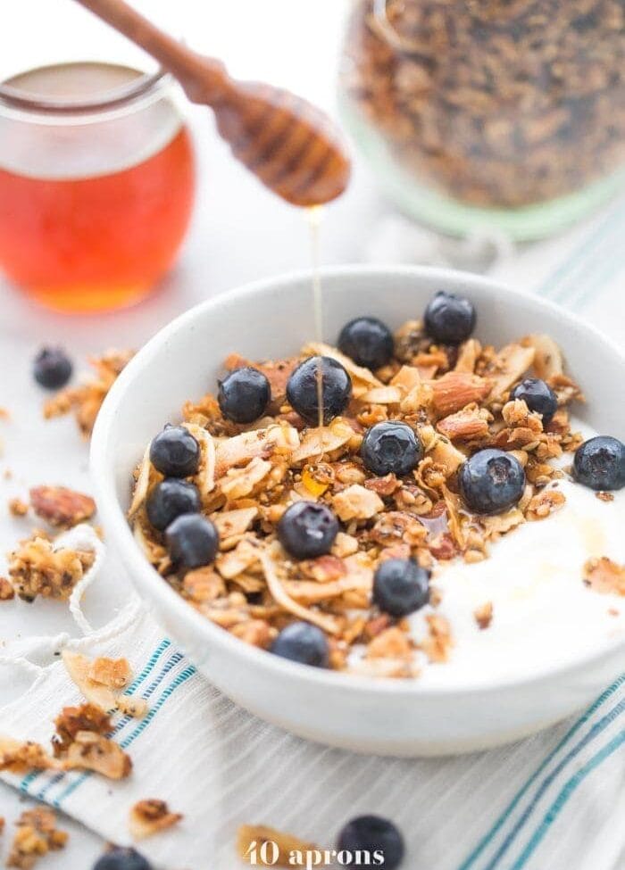 Bowl of the crunchy paleo granola recipe over yogurt, topped with blueberries and a drizzle of honey