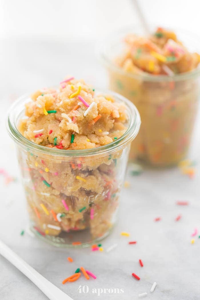 Side view of edible healthy cake batter dip (paleo and vegan) in glass jars with a spoon sticking out of the back jar.