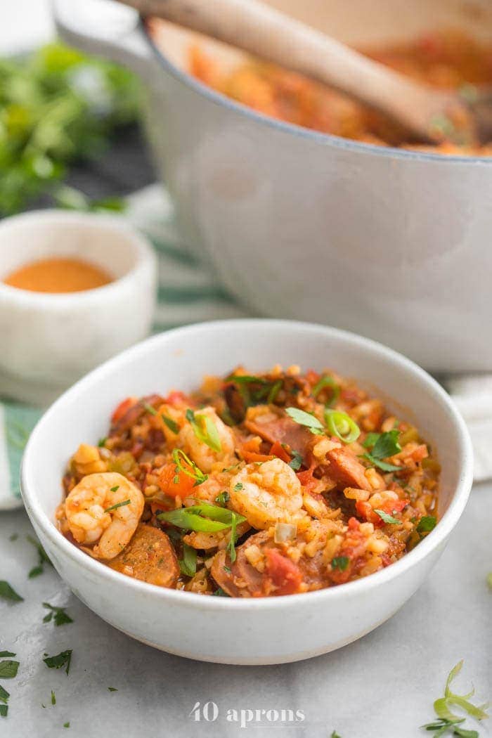 Whole30 healthy jambalaya with cauliflower rice in two bowls and a Dutch oven