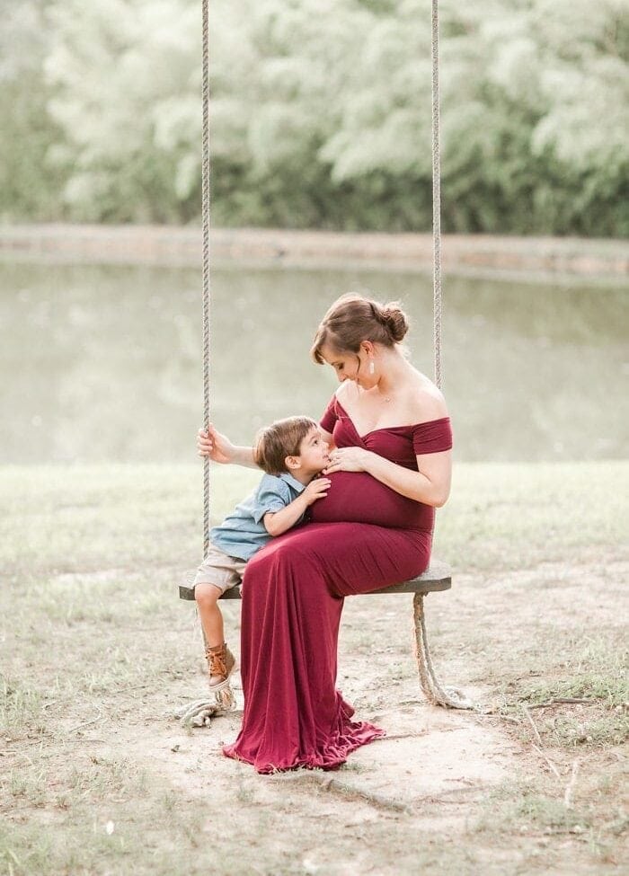 Toddler and pregnant mom on a swing in front of a lake