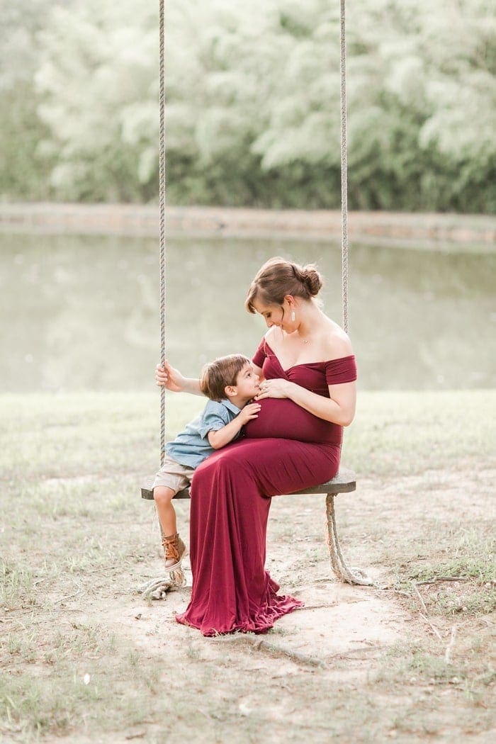 Toddler and pregnant mom on a swing in front of a lake