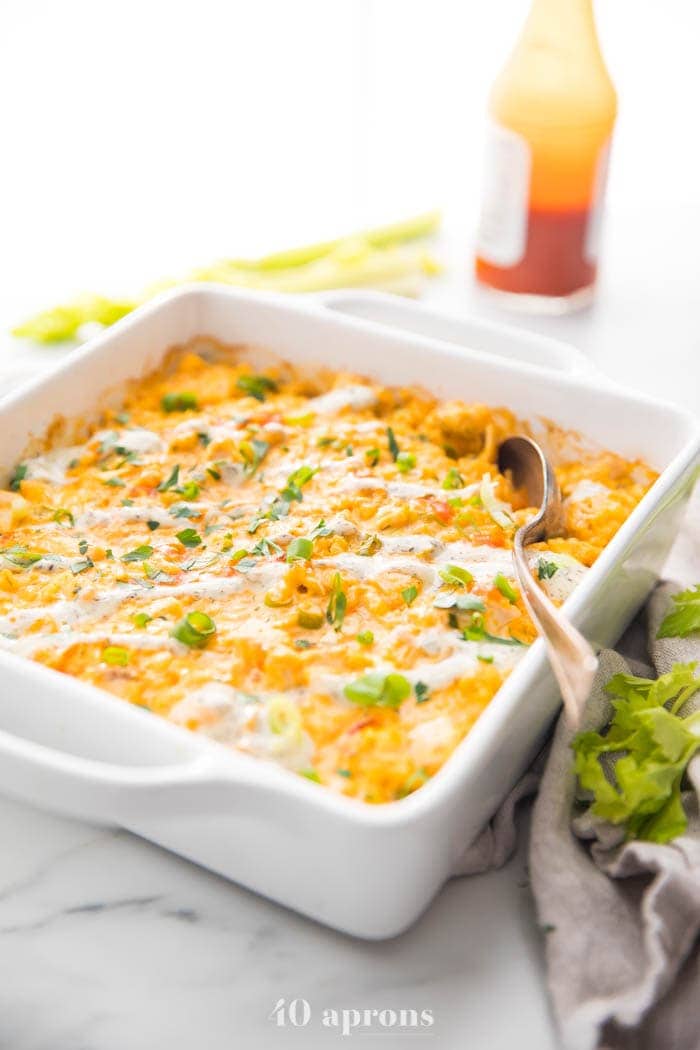 Paleo buffalo chicken casserole in a white dish with celery stalks and hot sauce in the background