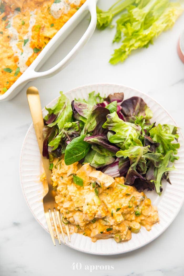 Paleo buffalo chicken casserole on a plate with salad and baking dish in the back