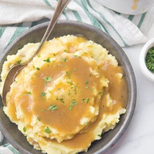 bowl of creamy mashed potatoes topped with a rich Paleo Gravy and some chopped chives