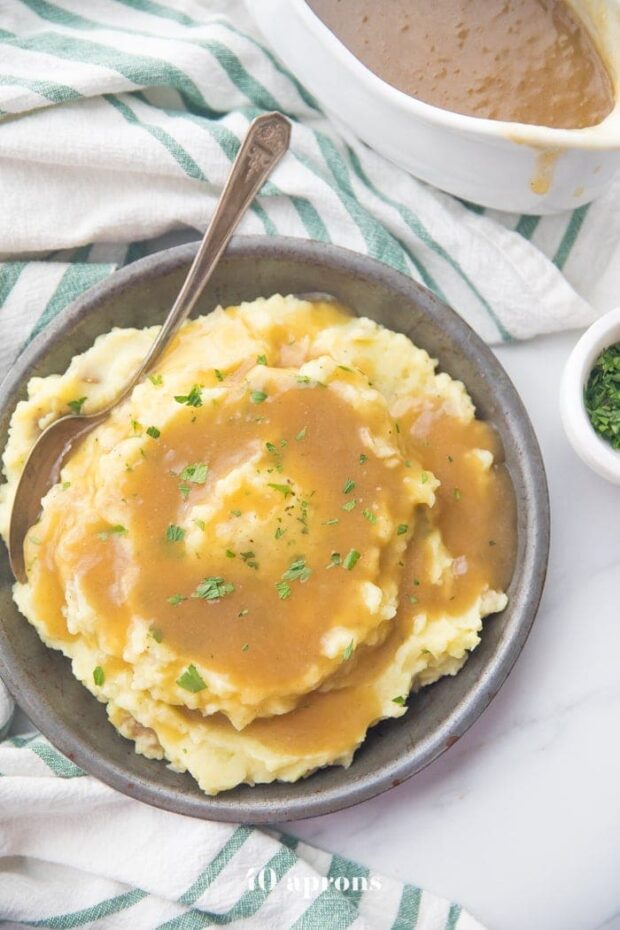 bowl of creamy mashed potatoes topped with a rich Paleo Gravy and some chopped chives