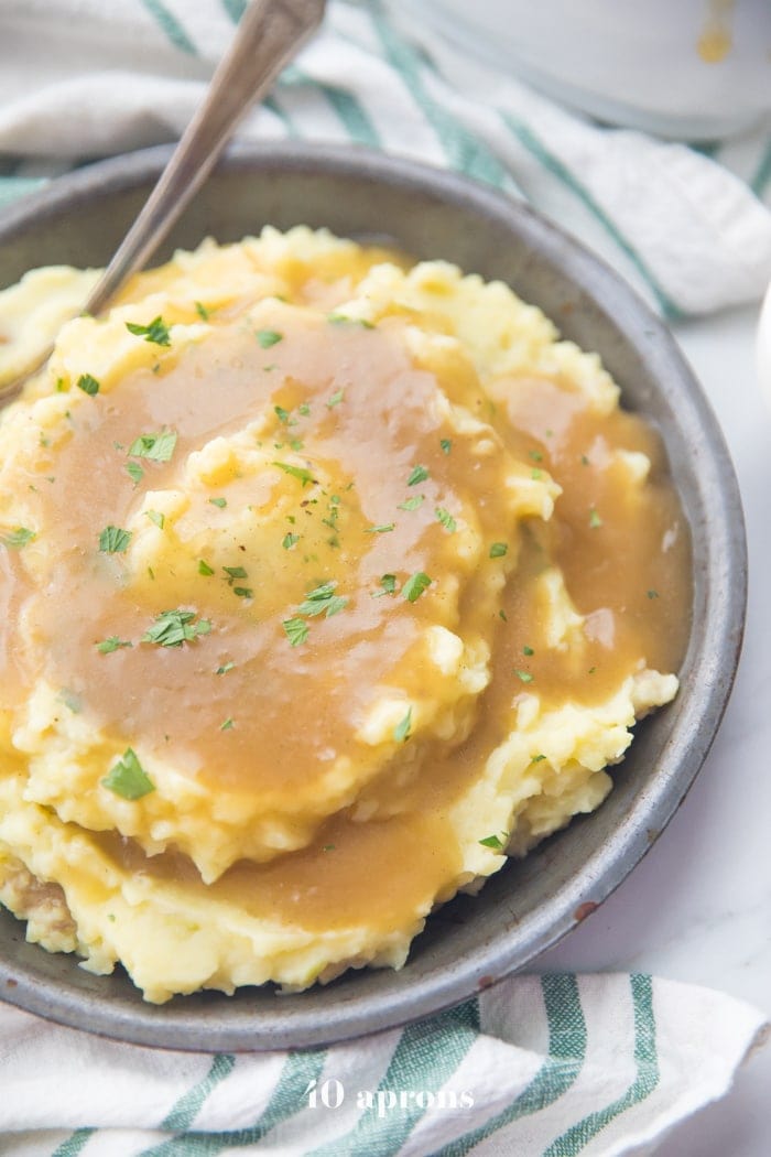  fluffy creamy mashed potatoes topped with a rich Paleo Gravy and some chopped chives served in a grey bowl
